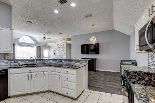 kitchen featuring stainless steel microwave, a sink, black dishwasher, visible vents, and vaulted ceiling