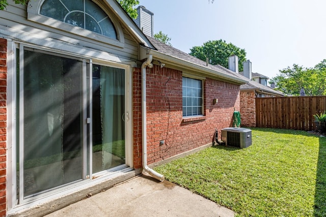 view of side of property featuring a chimney, a lawn, fence, central AC, and brick siding