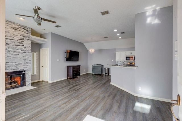 unfurnished living room with lofted ceiling, a textured ceiling, a fireplace, wood finished floors, and a ceiling fan