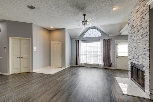 unfurnished living room featuring wood finished floors, ceiling fan, a stone fireplace, visible vents, and lofted ceiling