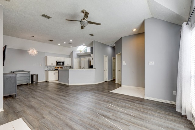 unfurnished living room with ceiling fan, lofted ceiling, visible vents, baseboards, and wood finished floors