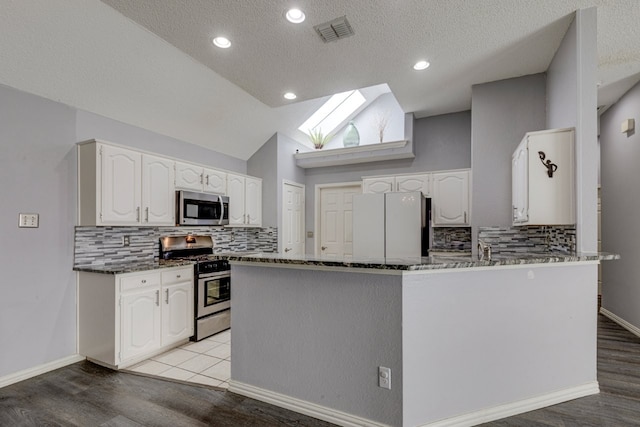 kitchen featuring dark stone countertops, stainless steel appliances, white cabinetry, visible vents, and a peninsula