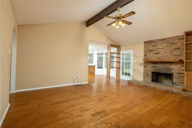 unfurnished living room featuring a brick fireplace, a ceiling fan, arched walkways, and wood finished floors