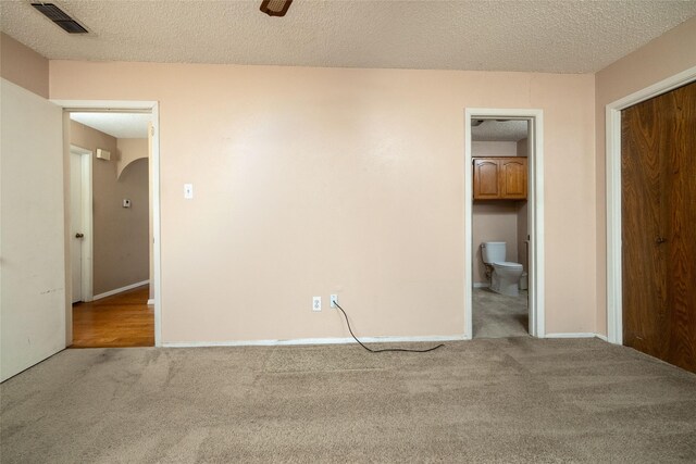 unfurnished bedroom with carpet flooring, arched walkways, a textured ceiling, and visible vents