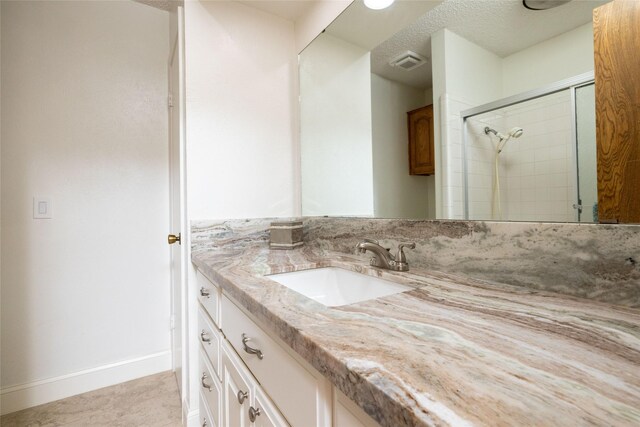 full bath featuring a textured ceiling, visible vents, a tile shower, vanity, and baseboards