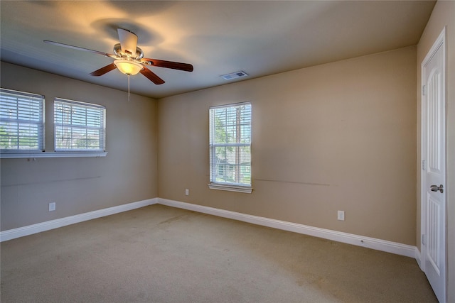 carpeted spare room with visible vents, baseboards, and a ceiling fan
