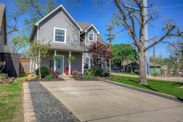 traditional home with a front lawn, fence, and a shingled roof