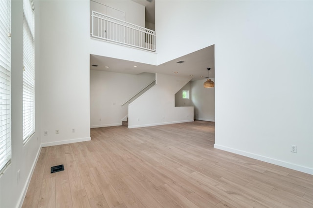 3251 Cambrick St Unit 13, Dallas, TX 75204 - unfurnished living room with a high ceiling, visible vents, baseboards, light wood-style flooring, and stairs