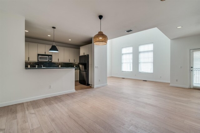3251 Cambrick St Unit 13, Dallas, TX 75204 - kitchen with stainless steel microwave, light wood finished floors, visible vents, and freestanding refrigerator