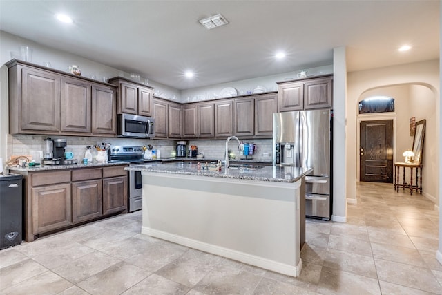 kitchen with stainless steel appliances, visible vents, a sink, light stone countertops, and decorative backsplash