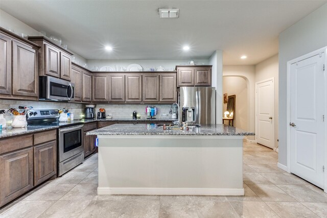 kitchen with arched walkways, visible vents, dark stone counters, and stainless steel appliances