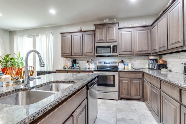 kitchen featuring stainless steel appliances, a sink, backsplash, and light tile patterned floors