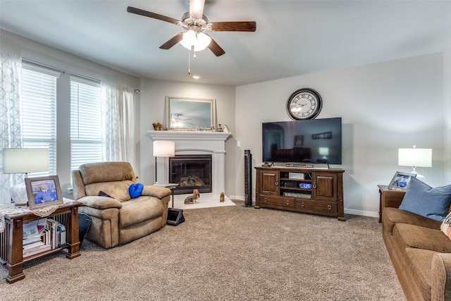 carpeted living room with a glass covered fireplace, a ceiling fan, and baseboards