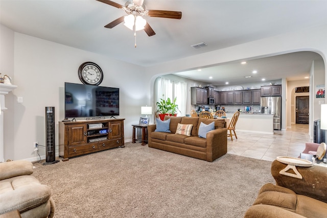 living area with a ceiling fan, arched walkways, light colored carpet, baseboards, and visible vents