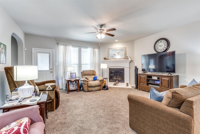 carpeted living area with arched walkways, a glass covered fireplace, and ceiling fan