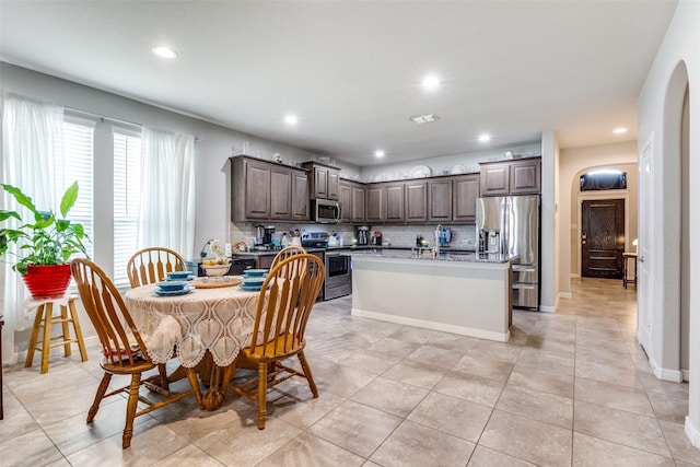 dining area with light tile patterned floors, arched walkways, baseboards, and recessed lighting