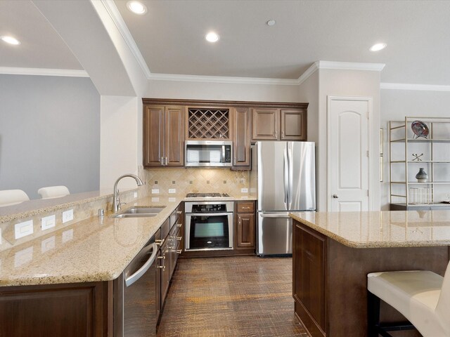 kitchen with crown molding, a peninsula, light stone counters, a sink, and appliances with stainless steel finishes