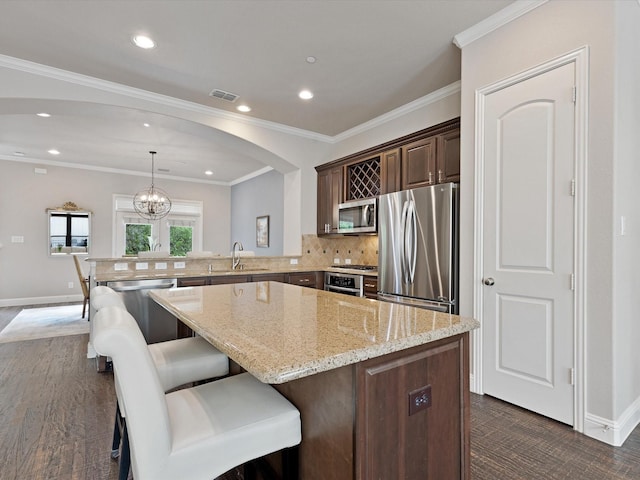 kitchen with light stone countertops, appliances with stainless steel finishes, a peninsula, backsplash, and visible vents