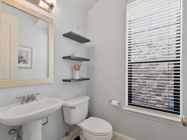 half bathroom featuring toilet, baseboards, and a sink