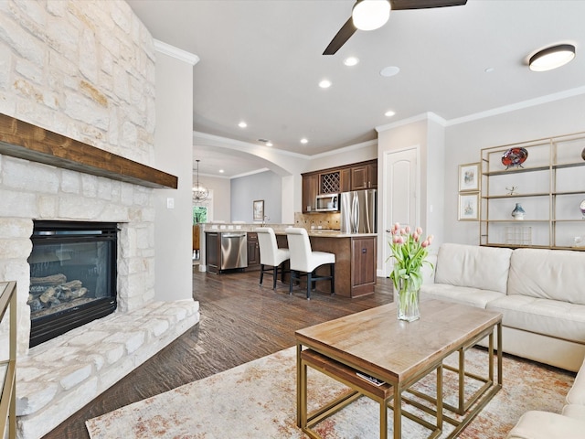 living area featuring crown molding, dark wood-style flooring, a stone fireplace, ceiling fan, and recessed lighting