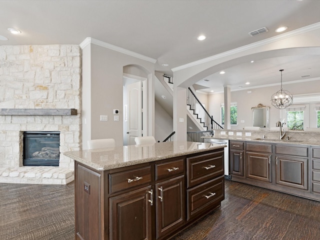 kitchen with light stone counters, a sink, a fireplace, dishwasher, and ornamental molding