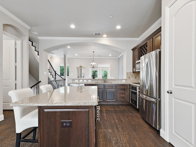 kitchen with a breakfast bar, a sink, arched walkways, stainless steel appliances, and visible vents
