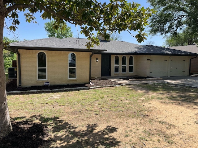 view of front of home with concrete driveway, a front lawn, brick siding, a garage, and central AC unit