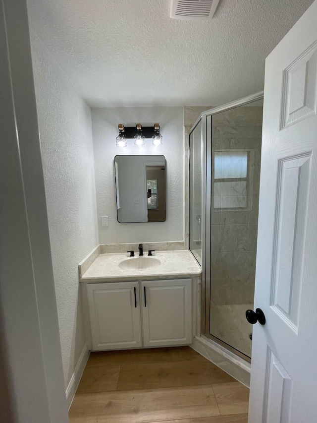 full bath featuring vanity, a textured ceiling, a shower stall, visible vents, and wood finished floors
