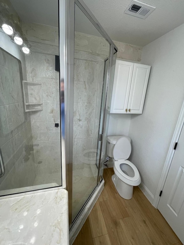 bathroom featuring visible vents, toilet, a shower stall, and wood finished floors
