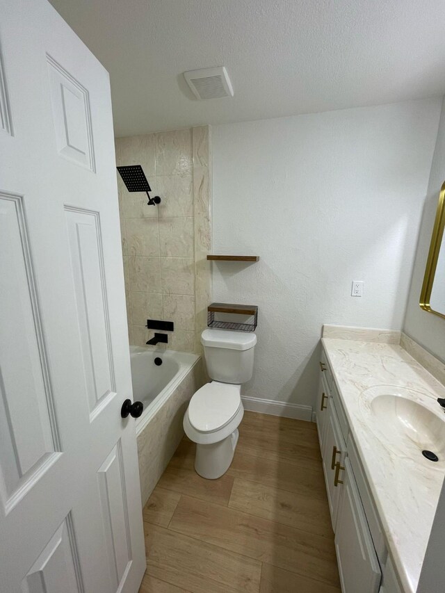 full bath with baseboards, toilet, vanity, wood finished floors, and tiled shower / bath combo