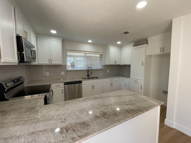 kitchen featuring a sink, a textured ceiling, wood finished floors, stainless steel appliances, and light stone counters