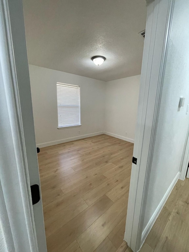 empty room with a textured ceiling, light wood finished floors, baseboards, and visible vents