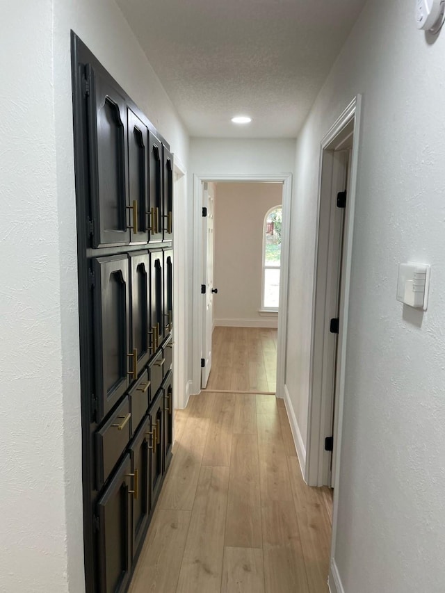 hall featuring baseboards, light wood finished floors, and a textured ceiling