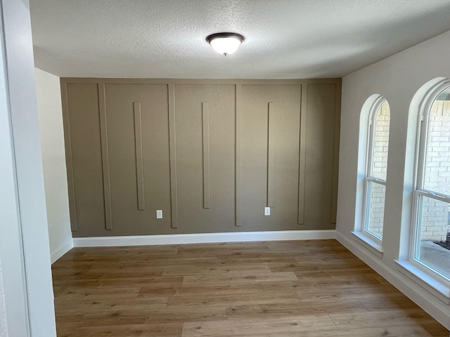 unfurnished room with light wood-style flooring, baseboards, and a textured ceiling