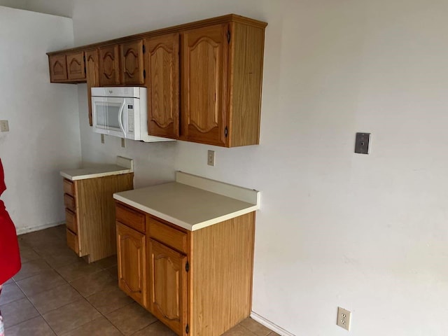 kitchen featuring white microwave, light countertops, brown cabinetry, and light tile patterned flooring