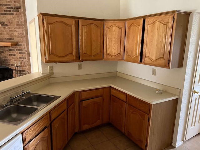 kitchen featuring light tile patterned flooring, light countertops, a sink, white dishwasher, and brown cabinets