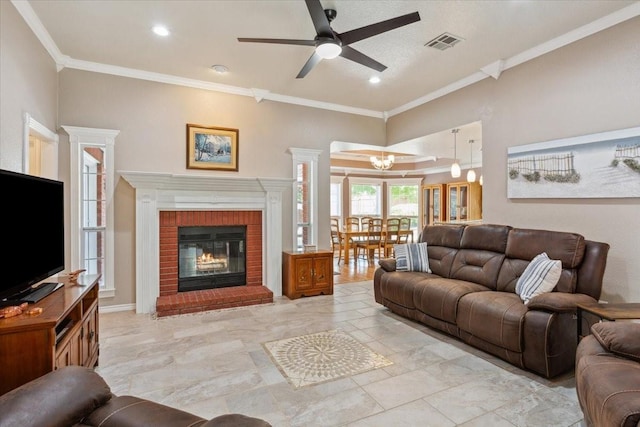 living room featuring crown molding, visible vents, a fireplace, and ceiling fan with notable chandelier