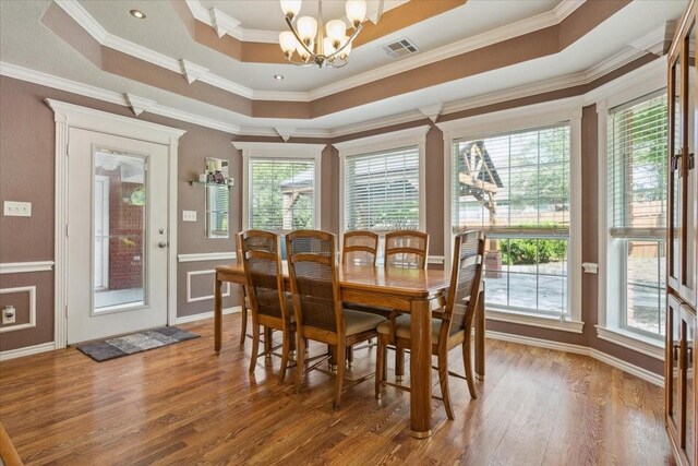dining room featuring a tray ceiling, ornamental molding, visible vents, a chandelier, and wood finished floors