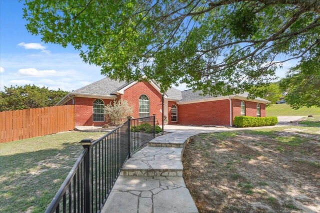 view of front of property featuring brick siding, a front yard, fence, and roof with shingles
