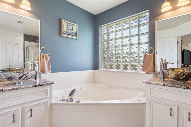 bathroom with two vanities, visible vents, a sink, a jetted tub, and a textured wall