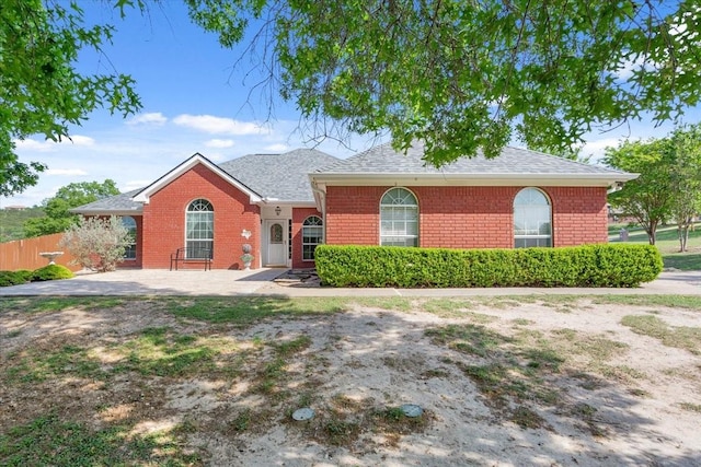 view of front of property featuring brick siding, fence, and a shingled roof