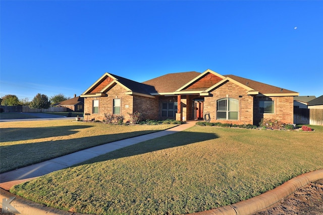ranch-style house featuring brick siding, a front lawn, fence, and roof with shingles