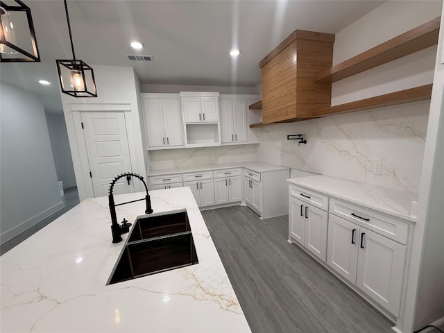 kitchen featuring backsplash, open shelves, light stone countertops, visible vents, and a sink