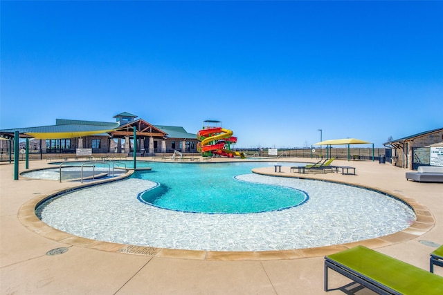 community pool with a patio area, fence, and a water slide
