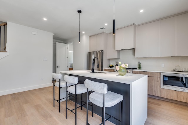 7312 Flyers Way, Dallas, TX 75235 - kitchen with modern cabinets, stainless steel appliances, a breakfast bar area, an island with sink, and light wood-style floors