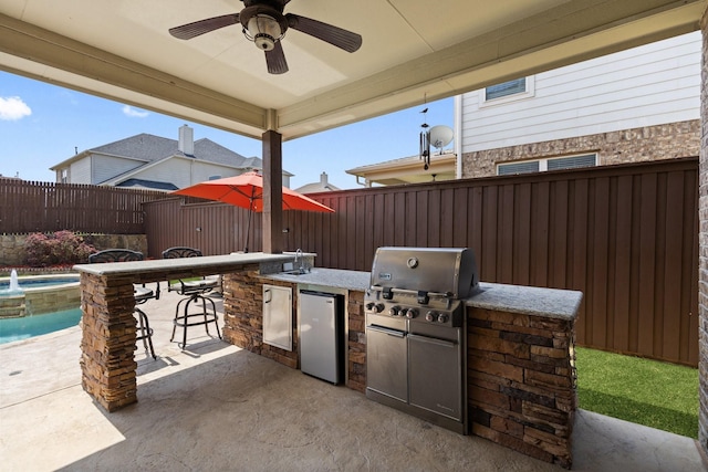 view of patio featuring outdoor wet bar, a ceiling fan, a fenced backyard, a grill, and an outdoor kitchen