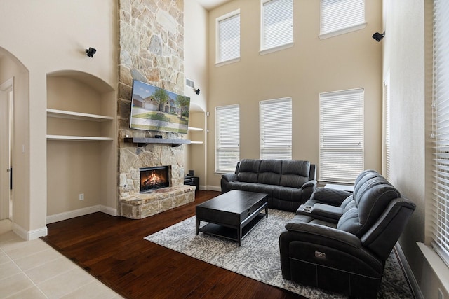 living room featuring built in features, wood finished floors, and a stone fireplace