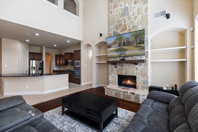 living area with visible vents, built in shelves, arched walkways, a stone fireplace, and light wood-style floors
