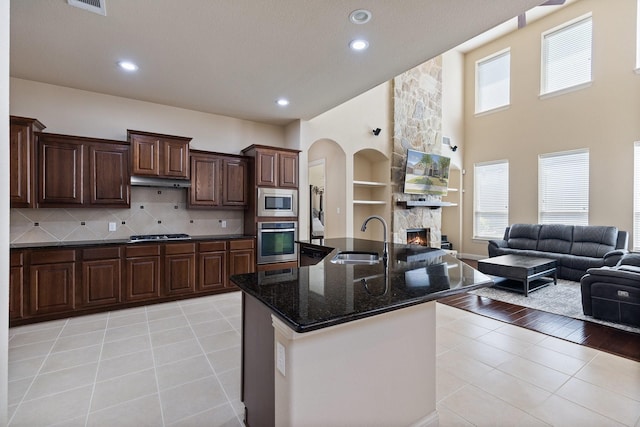 kitchen with under cabinet range hood, light tile patterned floors, a sink, appliances with stainless steel finishes, and open floor plan