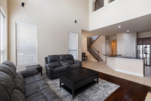 living room featuring light wood-style flooring, stairway, arched walkways, and a high ceiling